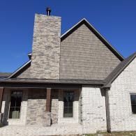 Brick house exterior with a tall stone chimney and steep gray roof under a clear blue sky