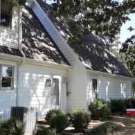 White house with steep gray roof, garage doors, and trees casting shadows in the yard