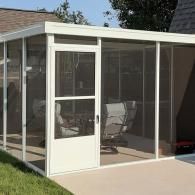 Screened patio enclosure with white frame and glass door, partially open on a sunny backyard patio