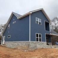 Blue two-story house with white trim and stone foundation on a cloudy day
