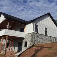 House under construction with stone and white siding, front porch, and ladders on a sloped lot