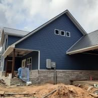 New blue house with stone foundation under construction, with dirt and building materials in front.