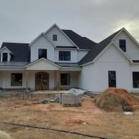 Large white house under construction with an unfinished front yard and building materials in front.