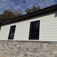 White house exterior with black-trim windows and a gray stone foundation under a blue sky