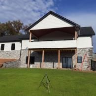 House with stone lower level, white upper siding, and a covered porch overlooking a green lawn