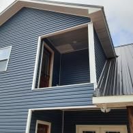 Blue house exterior with a second-floor balcony and open window near the roofline