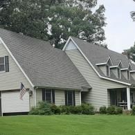 White suburban house with gray roof, green lawn, and large trees in front