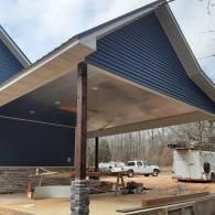 Covered patio under construction with dark blue siding, wood posts, and a white truck in the background