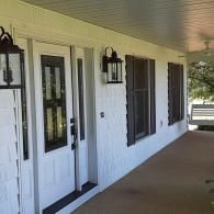 White house porch with French doors, black lanterns, and dark shutters along a covered walkway