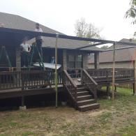 Wooden porch deck with stairs on a house, featuring railings and a covered roof in a grassy yard