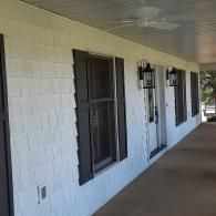 Covered porch with white brick walls, black windows, and a front door along a concrete walkway.