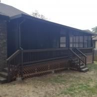 Dark wooden porch on a house with stairs and lattice skirting, set in a grassy yard.