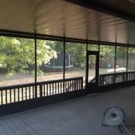 Covered porch with a view of a yard, wooden railing, and a small fan on the floor