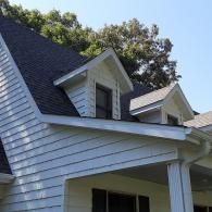 White house roof with two dormer windows against a blue sky and trees