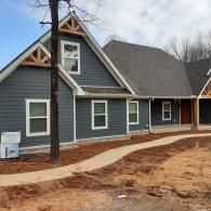Blue-gray house with white trim and a covered porch along a curved concrete walkway on a dirt lot