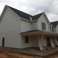 Gray house exterior under construction with front porch and black roof under cloudy sky