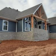 New suburban house with gray siding, stone facade, and red dirt front yard