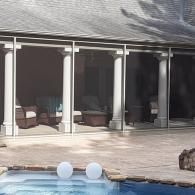 Patio with glass doors and potted plants beside a pool with two white floating balls