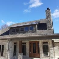 Stone house exterior with dormer windows and a tall chimney under a blue sky