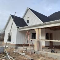 Partially built white house with black roof, porch scaffolding, and ladder on muddy construction site