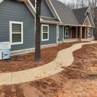Curved concrete walkway leading to a blue house with white trim and a red front door