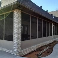 Screened porch with white brick exterior and gray roof beside a concrete walkway