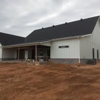 Single-story white house with dark roof and front porch on a dirt lot, overcast sky