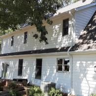 White two-story house with black shutters and a shaded front yard