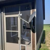 Satellite dish mounted on a small shed beside a grassy field