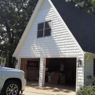 White detached garage with open door, driveway, and a silver truck parked at left.