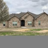 Brick suburban house with three gables, arched front door, and cloudy sky overhead