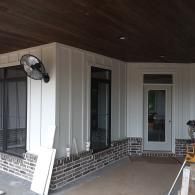 Covered porch with white siding, brick trim, a wall fan, and a glass door.