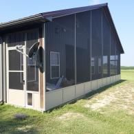 Screened porch on a dark gray building with a light door, windows, and grassy yard.