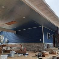 Blue house exterior with covered porch, brick foundation, and construction materials on the ground