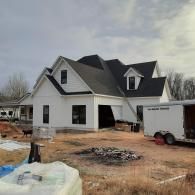 New white house under construction with dark roof and trailer in front
