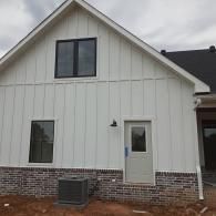 White house exterior with brick base, gray siding, and a small window by the front door.