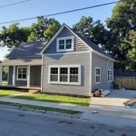 Gray house with white trim and front porch on a sunny residential street