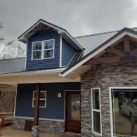 Blue house exterior with stone and wood siding, front porch, and dormer window