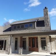 Stone house exterior with dormer windows, front porch, and tall chimney under a blue sky
