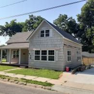 Gray house with white trim, front porch, and driveway on a sunny residential street.