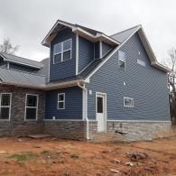 Blue two-story house with stone foundation and white trim on a bare lot