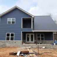 Partially built blue house with gray metal roof and unfinished front yard