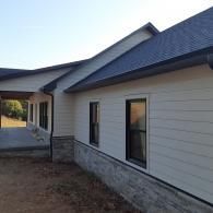 Side view of a house exterior with beige siding, stone foundation, and a covered walkway.