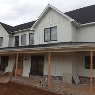 Modern two-story house with white siding and a covered porch under construction, with unfinished exterior and bare ground.