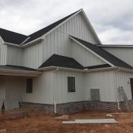 Exterior of a gray house under construction with steep gabled roof and red dirt yard