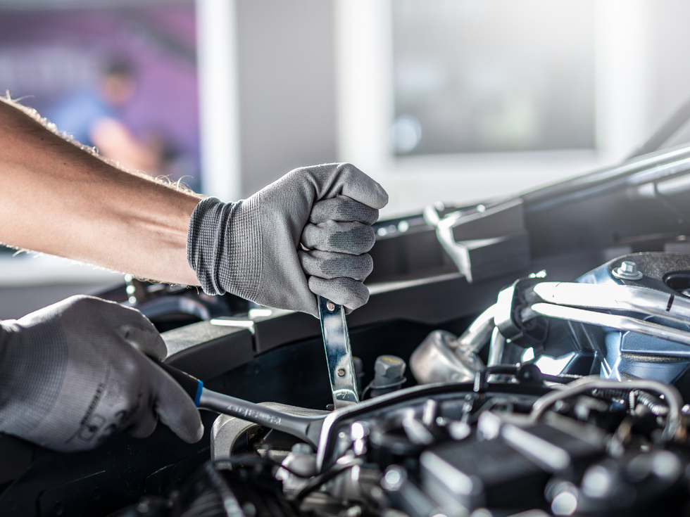Gloved hands using a wrench to repair a car engine under the hood