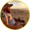 Person relaxing in a beach chair under a hat, looking out over the ocean at sunset