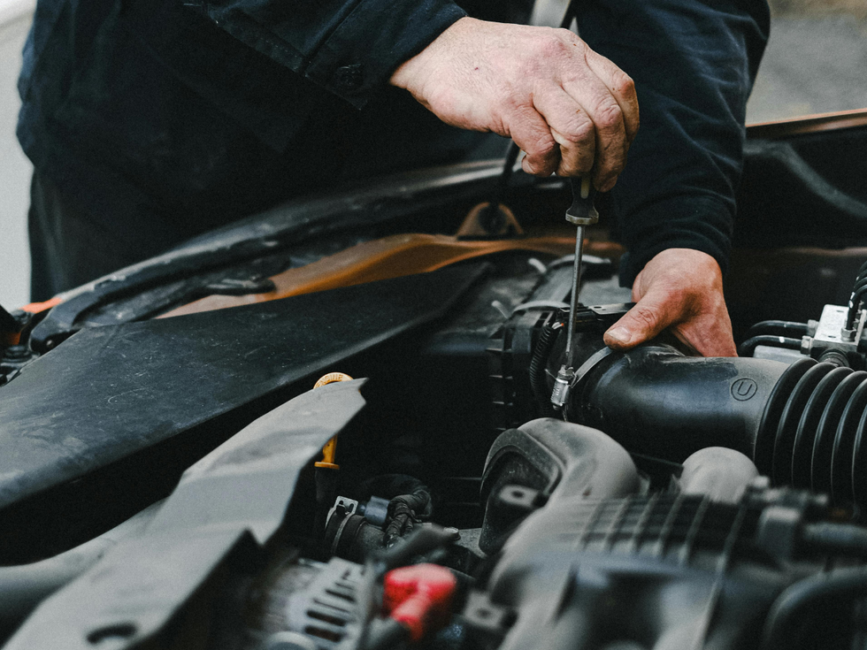 Mechanic working under an open car hood, using tools to repair the engine