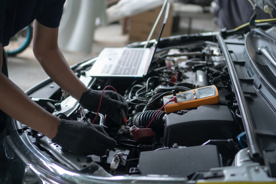 Mechanic working on a car engine with the hood open in a garage