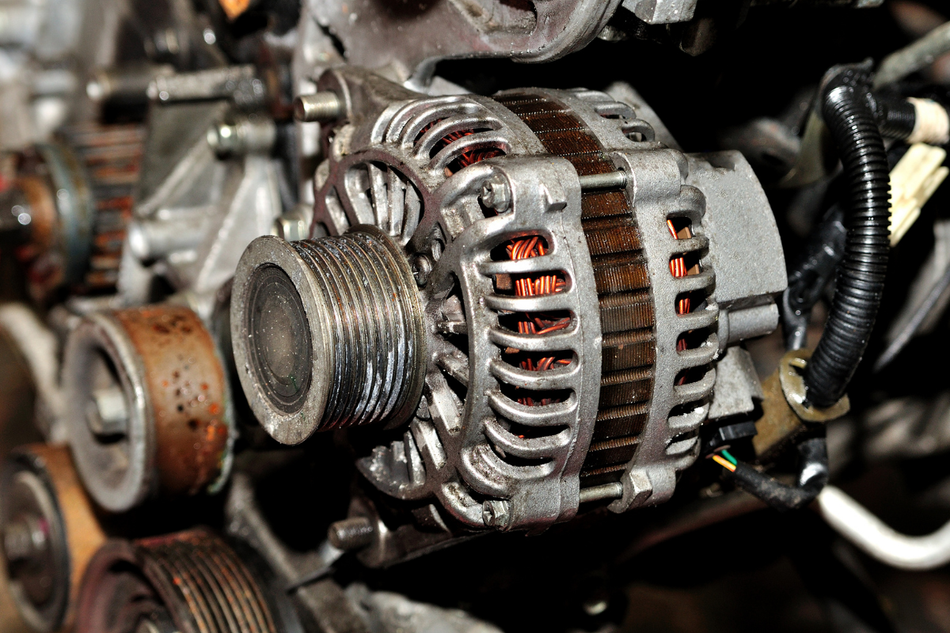 Close-up of a dirty car alternator with visible copper coils and pulley in an engine bay